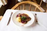 Gebratene Ente mit einem Kartoffelknödel und Blaukraut auf einem Tisch mit weißer Tischdecke im Spatenhaus in München
