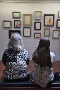 Zwei sitzende Frauen betrachten eine Wand mit Gemälden