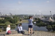 Drei Touristen auf der Aussichtsplattform des Olympiabergs mit Blick auf den Park und das Hinterland.