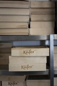 Holzboxen mit dem Käfer Logo liegen gestapelt in einem Regal.