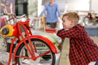 Kind mit kariertem Hemd schaut sich im Verkehrszentrum ein historisches Motorrad aus der Nähe an.