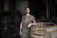 Der Münchner Fassmacher Peter Schmid in lederner Arbeitsschürze lehnt an einem großen renovierungsbedürftigen Fass.
