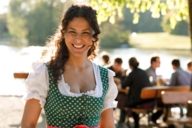 Eine Frau im Dirndl steht im Abendlicht in einem Biergarten in München und lacht.