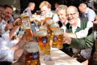 Ein Tisch mit Männern prostet sich im Biergarten des Hofbräuhauses in München zu.