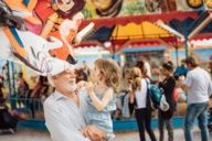 Ein älterer Herr mit grauen Haaren trägt seine Enkelin über die Auer Dult in München.