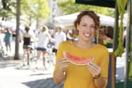 Eine Frau in einem gelben Pullover isst eine Melone am Viktualienmarkt.