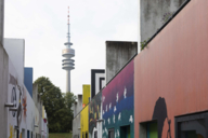 Bunte Bungalows im Olympischen Dorf München mit dem Olympiaturm im Hintergrund