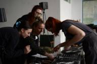 Vier Frauen lehnen über einem DJ-Equipment und arbeiten daran.