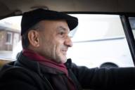 Ein Mann mit Schildmütze sitzt im Auto und lächelt.