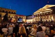 Au crépuscule, des gens sont assis sur la place Max Joseph devant le Théâtre national de Munich et regardent la retransmission d'un opéra sur un écran dans le cadre de l'événement « Opéra pour tous ».