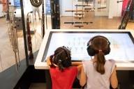 Zwei Mädchen hören sich auf dem Tablet des Deutschen Museums in München mit Kopfhörern die unterschiedlichen Instrumente an.