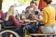 Eine Rollstuhlfahrerin und zwei weitere Personen sind im Biergarten Viktualienmarkt.