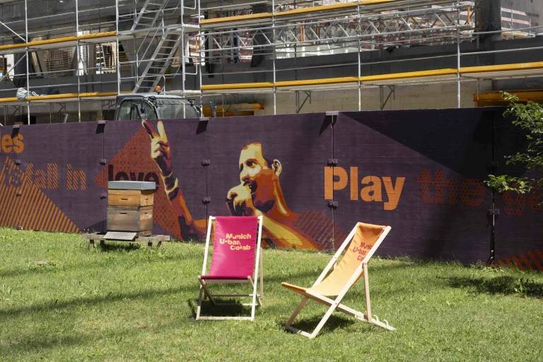 The outdoor area of the Munich Urban Colab, with deckchairs in front of a construction scaffold on which Freddie Mercury is painted.
