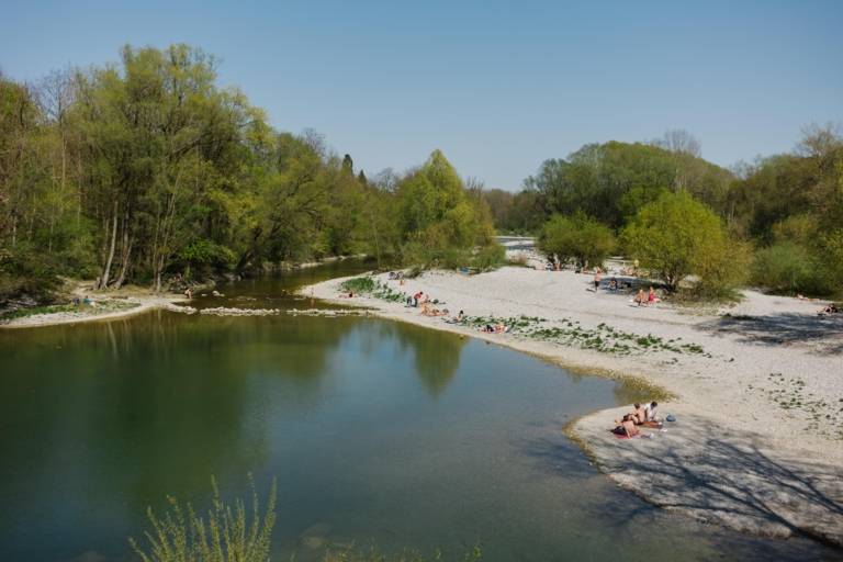Mehrere Menschen liegen in der Sonne am Isarstrand beim Flaucher in München