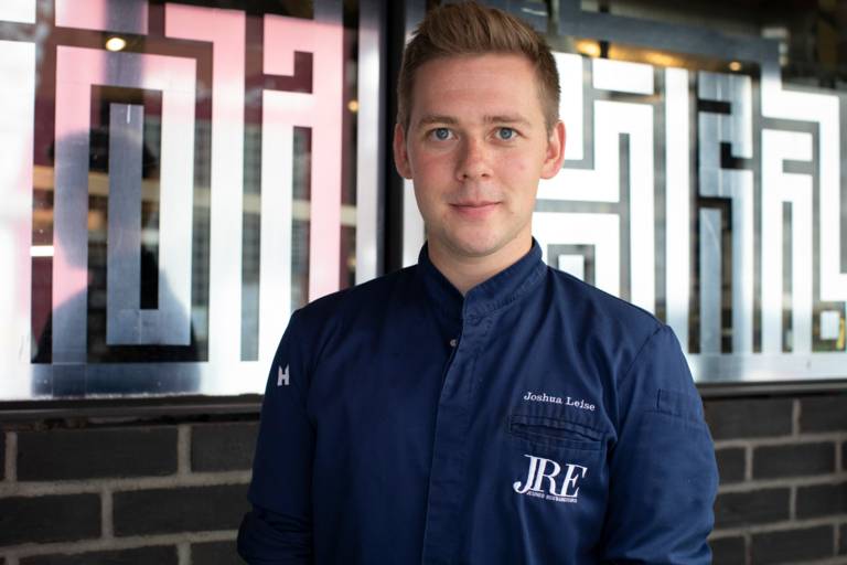 Der Sternekoch Joshua Leise steht in seiner blauen Kochjacke im Restaurant Mural