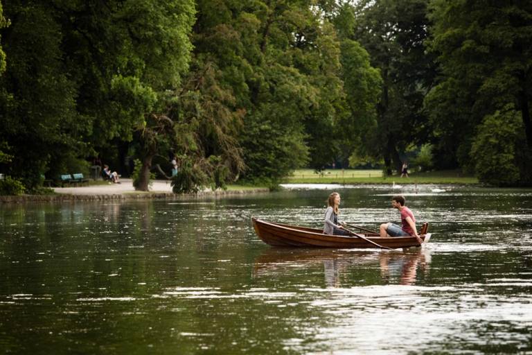 A couple is sitting in a rowboat on the lake in the Englische Garten in Munich.