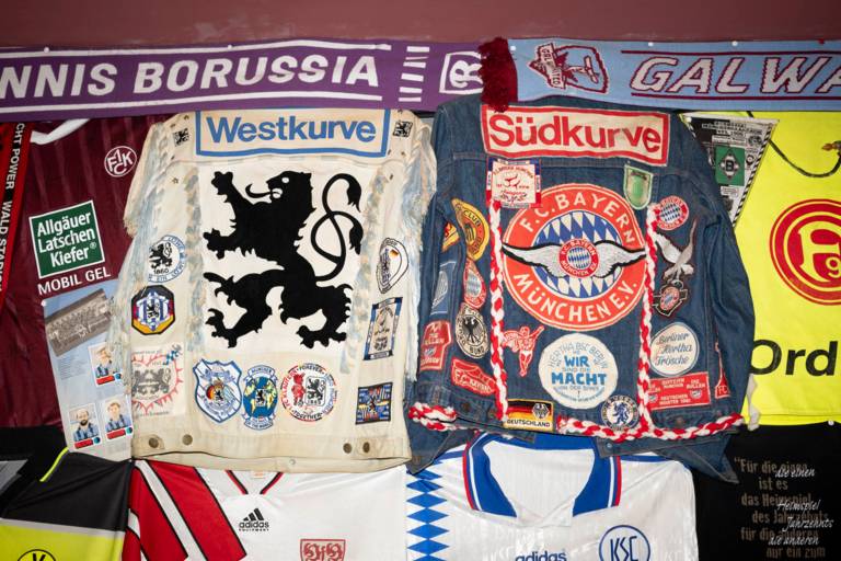 Historische Fußball-Fanartikel wie eine Jacke vom FC Bayern München mit verschiedenen Stickern und eine Jacke von 1860 München im gleichen Stil in München.