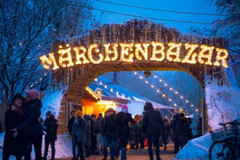 A wooden archway standing in the illuminated ‘Fairy Tale Bazaar’, under which people dressed for winter walk through.