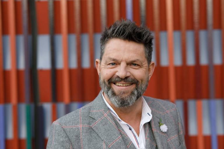 Ein lachender Mann mit Vollbart steht vor dem Museum Brandhorst in München.