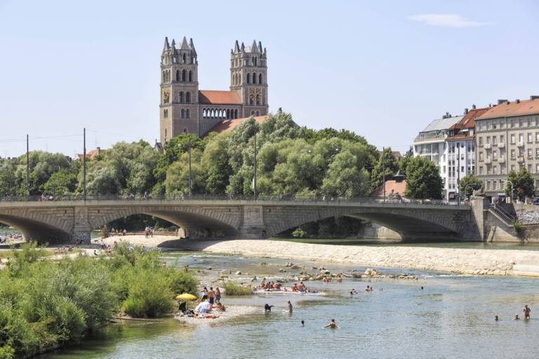 People swimming and sun bathing at the Isar river in München with the church St Maximilian in the background.