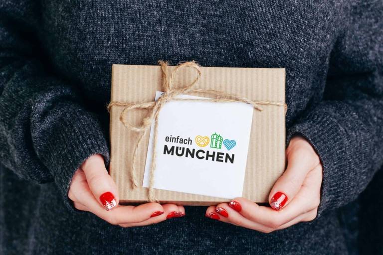 Eine Frau mit lackierten Fingernägeln hält ein Geschenk mit der Aufschrift „einfach München“
