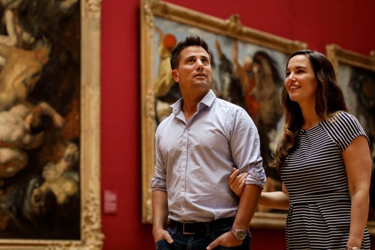 Ein Paar geht Arm in Arm durch die Alte Pinakothek in München und betrachtet die Gemälde.