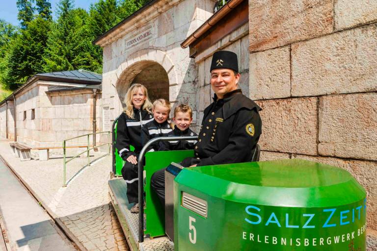 Mutter und zwei Kinder und ein Fahrer in der offenen grünen Grubenbahn des Salzbergwerks in Berchtesgaden
