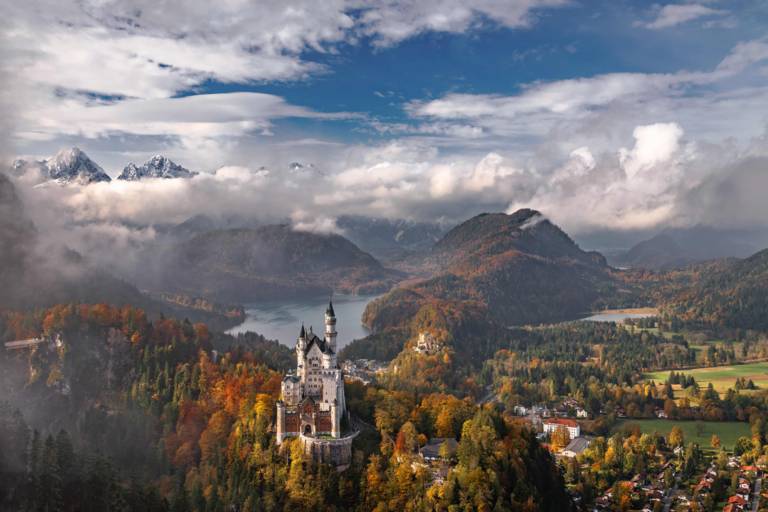 Das Schloss Neuschwanstein umrahmt von herbstlichen Wäldern und Bergen