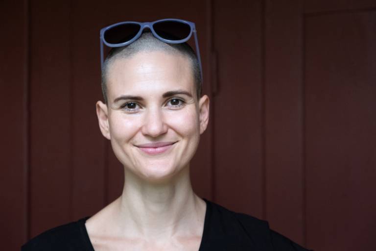 Author Elena Hell sits in front of red-painted panelling and smiles at the camera.
