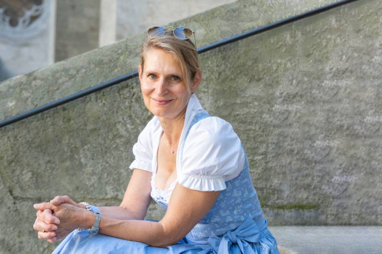 Carolin Engelhardt, founder and creative director of “Münchner Dirndl“-Manufaktur, is sitting on a staircase.