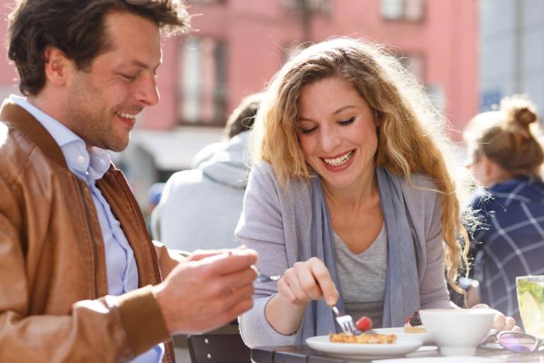 A couple is sitting in a street cafe and is eating cake at Gärtnerplatz in Munich.