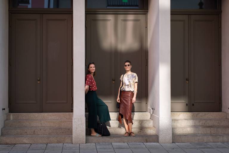 Zwei Frauen stehen vor drei großen Holztüren in München.
