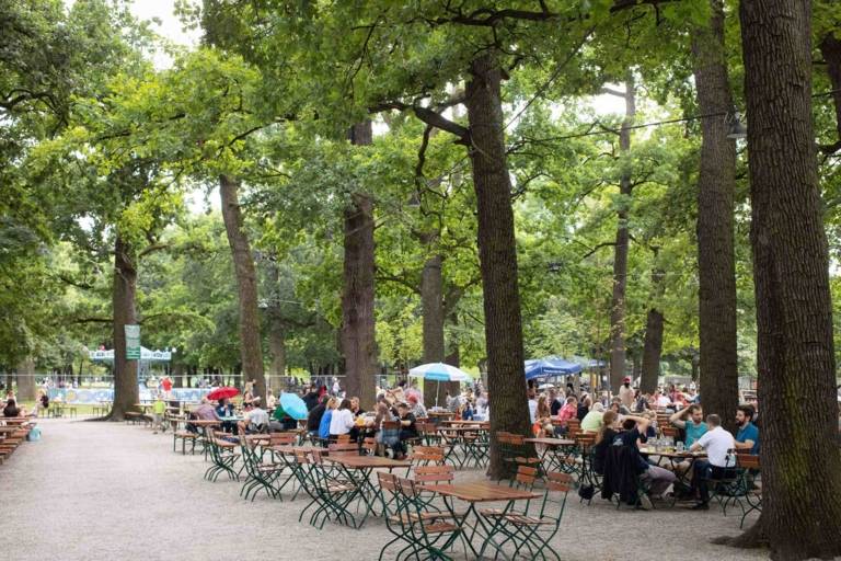 Gäste sitzen unter Kastanienbäumen im Biergarten Hirschgarten in München.