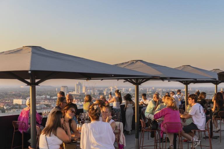 A few people are sitting on the roof terrace of the Otto 25 Rooftop Bar in Werksviertel-Mitte, watching the sunset