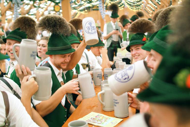 Trachtler sitzen auf der Bierbank und trinken Bier aus Krügen in München.