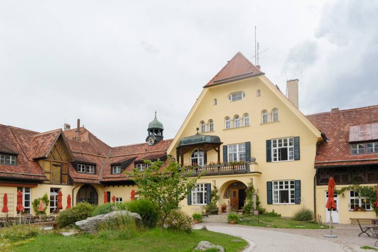 Exterior view of the Hotel Gut Sonnenhausen, an old brick house painted yellow with a front garden.