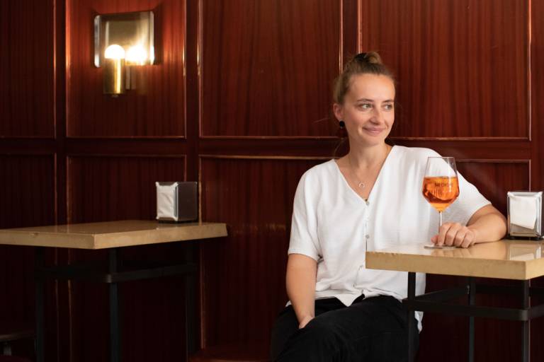 Junge Frau sitzt mit einem Glas Aperol Spritz in einer Bar in München.