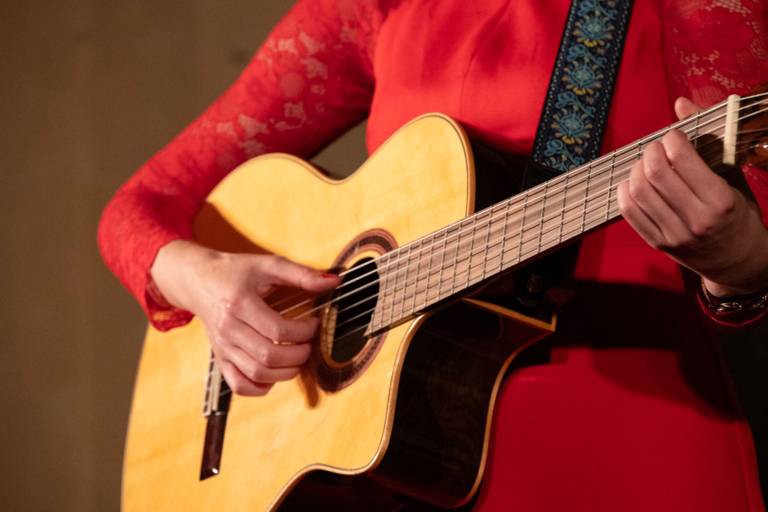 Die Kabarettistin Claudia Pichler steht auf einer Bühne und spielt auf einer Gitarre.