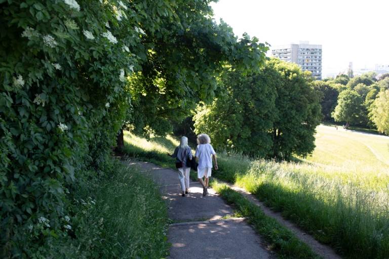 Ein Paar spaziert auf einem Weg im Luitpoldpark den Hügel hinab entlang grüner Wiesen.