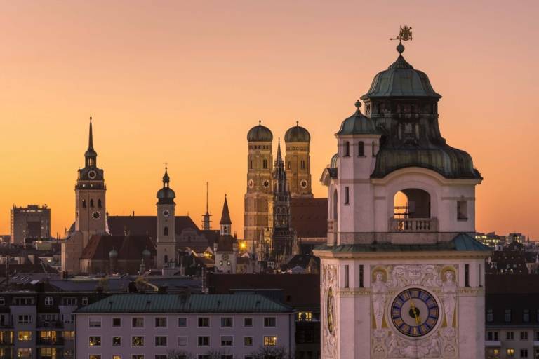 Panoramic view of the inner city of Munich at sunset with the Müllersches Volksbad in front and the towers of the Alter Peter, Heilig-Geist-Kirche and Frauenkirche in the background.